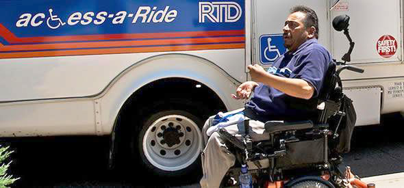 A man using a wheelchair getting ready to board an RTD bus with the Access-a-Ride logo on it.